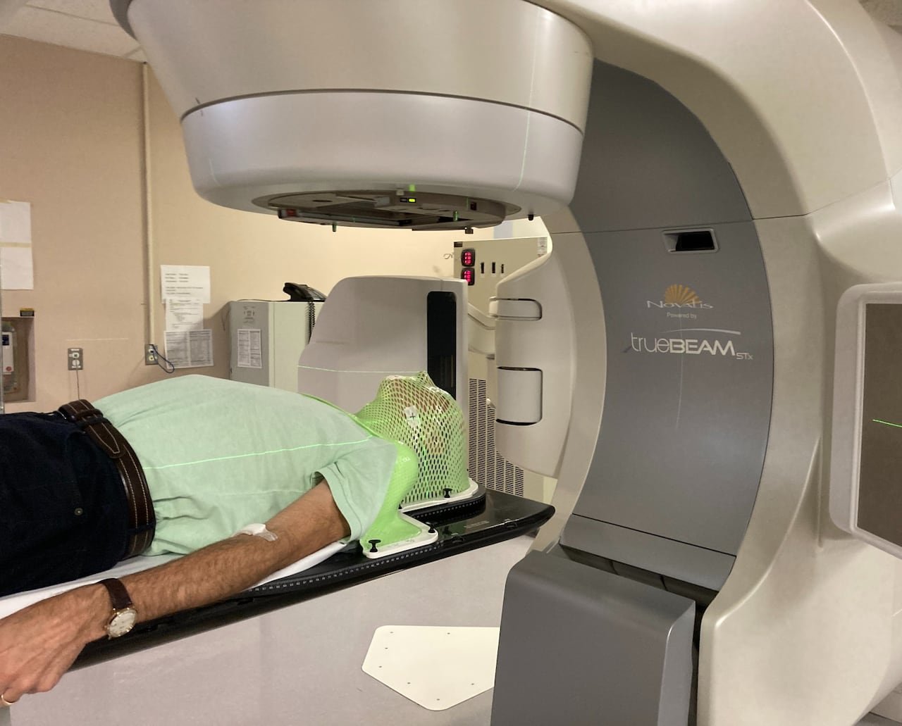 A man wearing a light shirt is covered with a plastic targeting mask and is underneath a scanner.