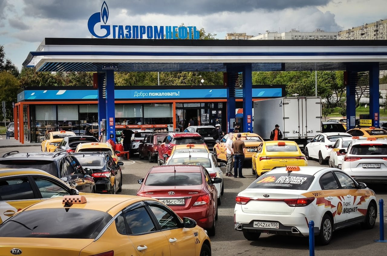 Several vehicles, including many yellow cabs, are shown in a parking lot of a gas station.