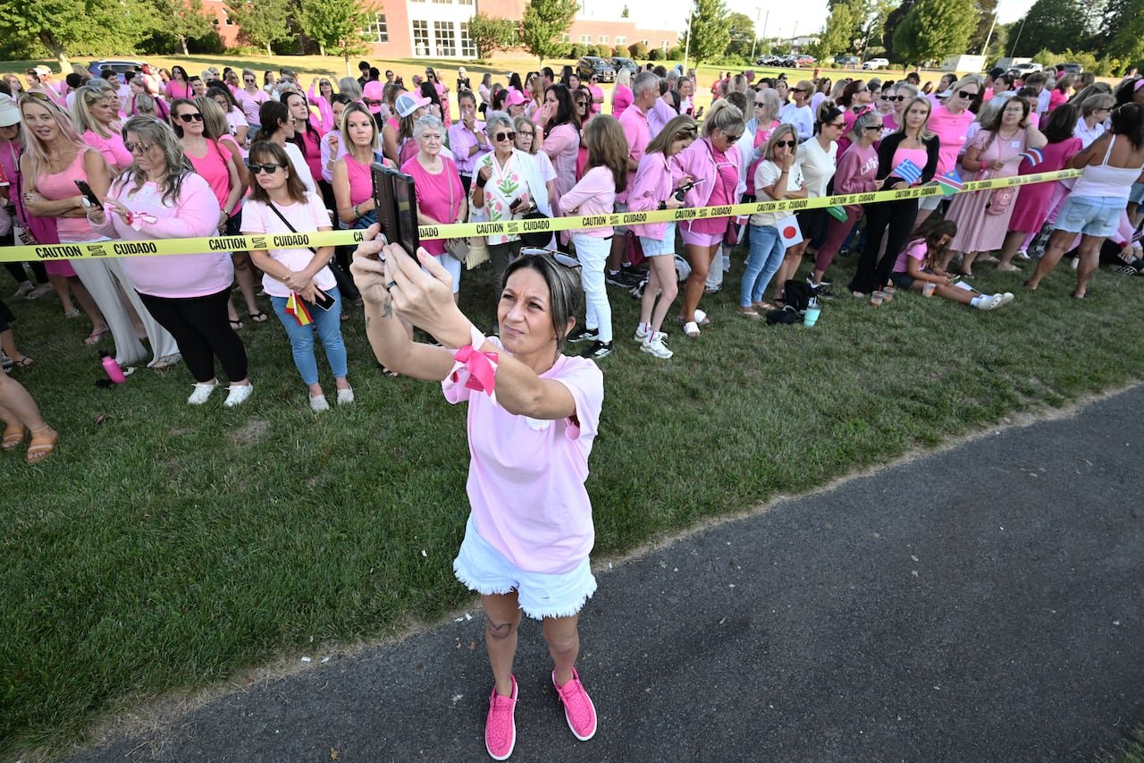 A woman in pink holds a phone in the air to record a large group of other women wearing pink standing outside a courthouse